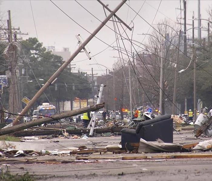 A street with damaged power lines, debris and emergency workers