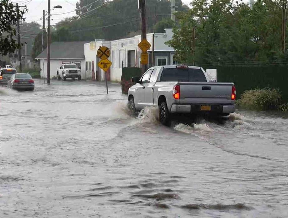 truck driving through a flooded roadway with a line of cars ahead