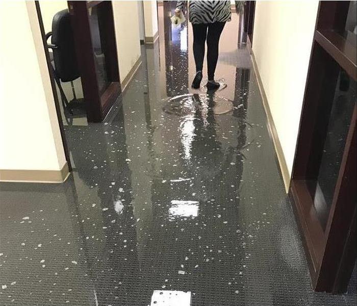 Person walking through standing water on a carpeted office hallway. 