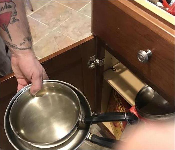 Hand pulling a pan out of a lower kitchen cabinet 